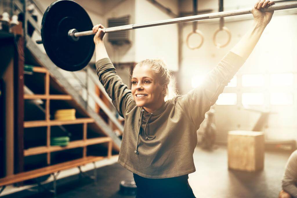 Smiling woman lifting barbell overhead